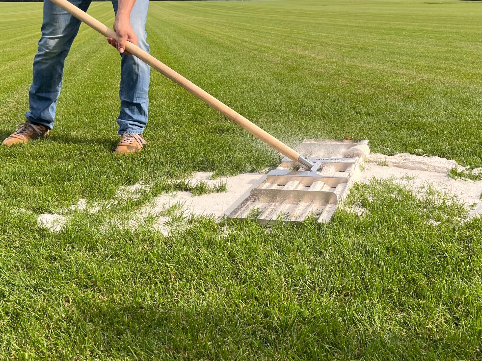 Ein Rasenrakel zum Planieren von Rasensand auf einem Rasen